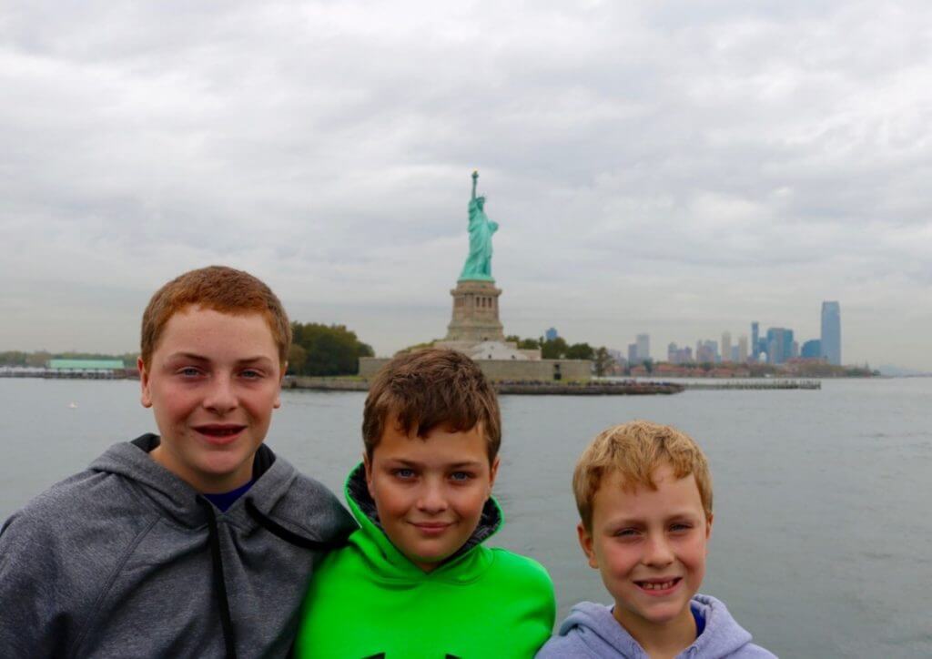 Three boys posing with Statue of Liberty behind them. 