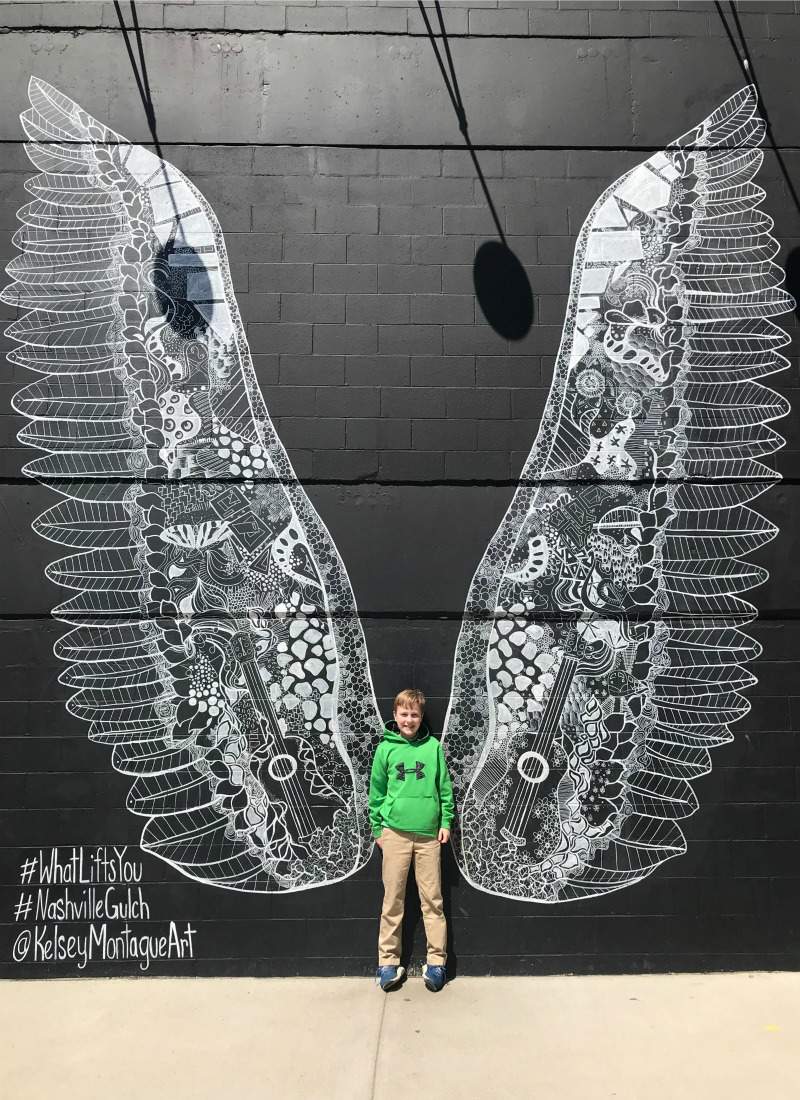 Boy standing in "What Lifts You" wings Nashville street art.